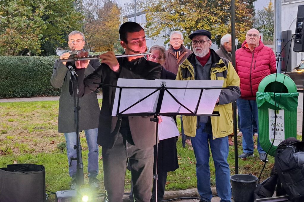 Ein Mann spielt auf einer Querflöte, dahinter eine Menschengruppe. Ein Mann spielt auf einer Querflöte, dahinter eine Menschengruppe.