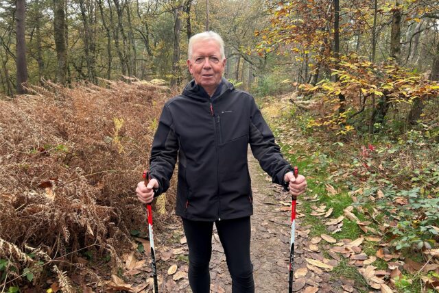Ein Mann in schwarzer Regenjacke und schwarzer Hose steht in der Haard. Seine Nordic Walking-Sticks hält er in den Händen.