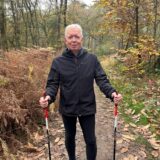 Ein Mann in schwarzer Regenjacke und schwarzer Hose steht in der Haard. Seine Nordic Walking-Sticks hält er in den Händen.