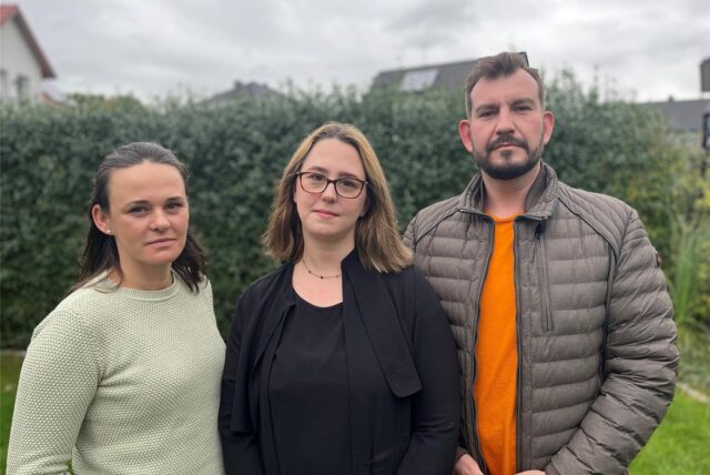 Zwei Mütter und ein Vater von Kita-Kindern aus Brackel stehen in einem Garten in Dortmund und schauen ernst in die Kamera.
