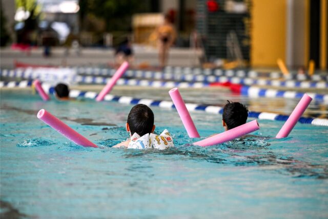 Kinder schwimmen mit Hilfe von Schwimmnudeln