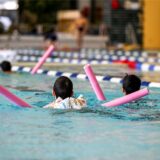 Kinder schwimmen mit Hilfe von Schwimmnudeln