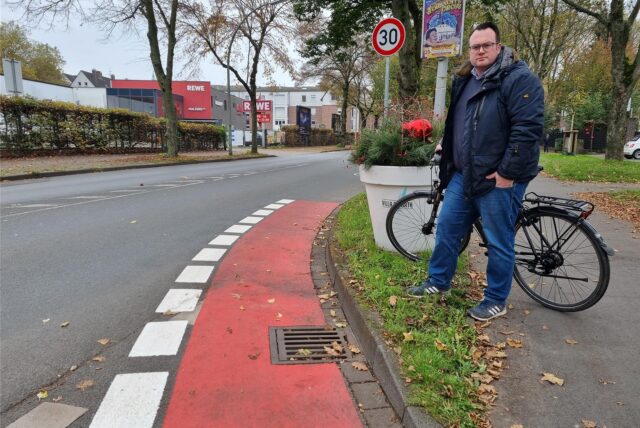 Ein Mann mit einem Fahrrad steht an einem Radweg.