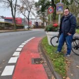 Ein Mann mit einem Fahrrad steht an einem Radweg.