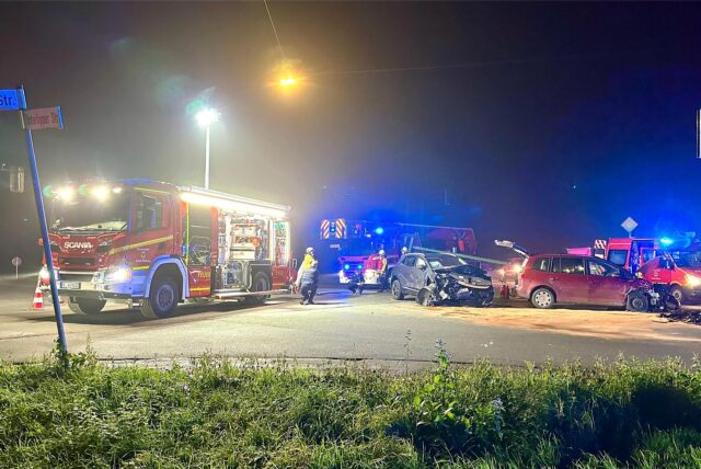 Zwei demolierte Autos stehen auf einer Kreuzung. Ein Feuerwehrfahrzeug parkt im Hintergrund und versperrt die Straße