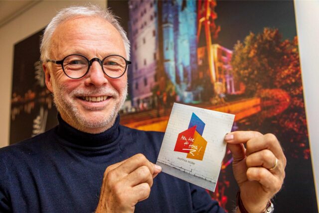 Bürgermeister Matthias Müller steht vor Fotos der ehemaligen Zeche Ewald und hält seine CD „Mein Lied für Herten“ in den Händen.