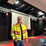 Ein Mann in gelber Sanitäterweste steht vor einer Bühne in der Realschule in Datteln.