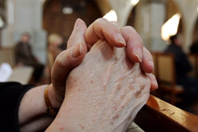 Eine Frau faltet am Buß- und Bettag in der Kirche die Hände zum Gebet.