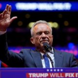 Robert F. Kennedy Jr. steht an einem Rednerpult mit der Aufschrift „Trump will fix it“ und hält den Arm in die Höhe.