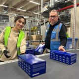 Christoph Brings, Standortleiter bei Arvato in Dorsten, steht neben einer Mitarbeiterin an einem Fließband, auf das die Bestellungen gelegt werden.
