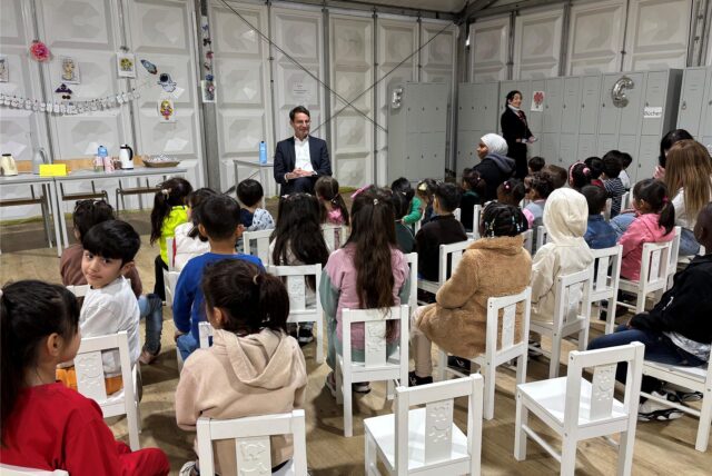 Regierungspräsident Andreas Bothe sitzt vor vielen Kindern, die auf weißen Stühlen sitzen.