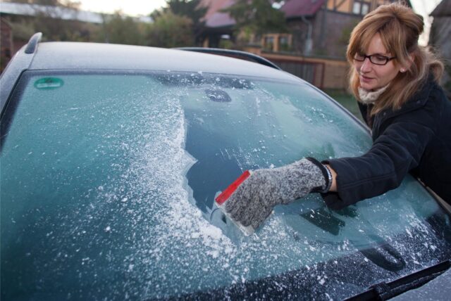 Eine Frau kratzt die Scheibe ihres Autos frei.
