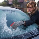 Eine Frau kratzt die Scheibe ihres Autos frei.