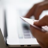 Finger tippen Bankdaten in eine Tastatur, die linke Hand hält eine Bankkarte
