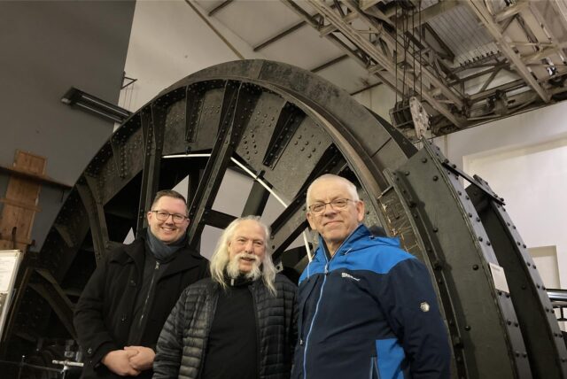 Vor der riesigen Treibscheibe der Fördermaschine der ehemaligen Schachtanlage Auguste Victoria 4 in Drewer stehen (v.l.) Johannes Jansen, Michael Heyder und Alfred Dodot.