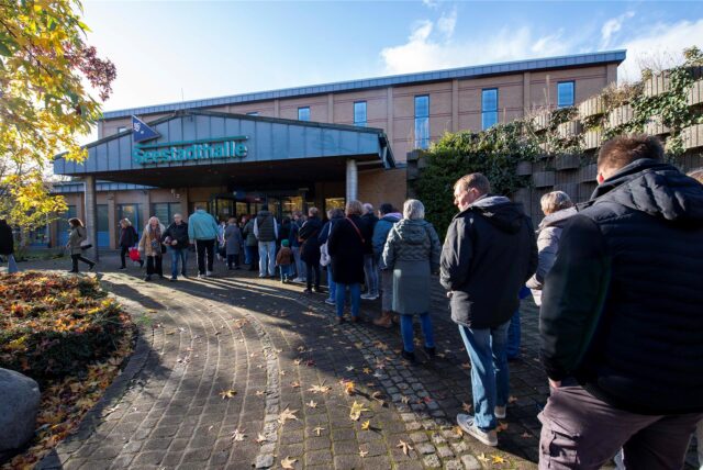 Menschen stehen in einer Schlange an der Seestadthalle.