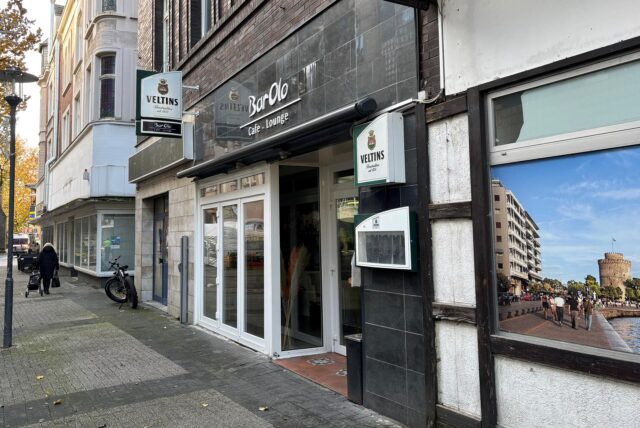 Die Außenseite des Hertener Lokals BarOlo auf der Antoniusstraße in der Innenstadt. Die Blick Richtung geht schräg in Richtung St. Antonius Kirche. Im Hintergrund läuft eine Passantin.