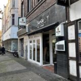 Die Außenseite des Hertener Lokals BarOlo auf der Antoniusstraße in der Innenstadt. Die Blick Richtung geht schräg in Richtung St. Antonius Kirche. Im Hintergrund läuft eine Passantin.
