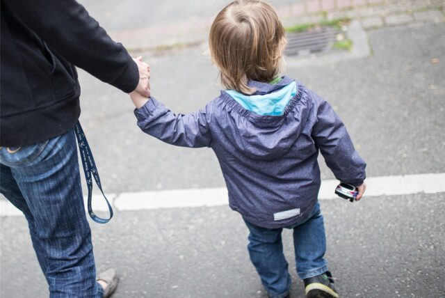 Eine erwachsene Person hält ein Kind an der Hand.