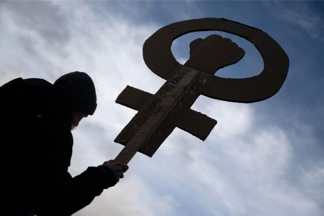 Eine Teilnehmerin einer Kundgebung hält auf dem Marktplatz ein Frauenzeichen mit einer Faust in der Hand.
