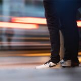 Eine Person mit weißen Turnschuhen wartet am Rande einer Straße.