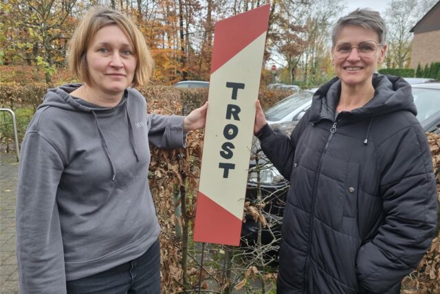 Irene Müllender und Katrin Tüllmann stehen vor einem Schild, auf dem das Wort Trost steht.