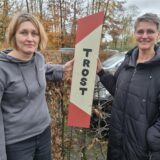 Irene Müllender und Katrin Tüllmann stehen vor einem Schild, auf dem das Wort Trost steht.