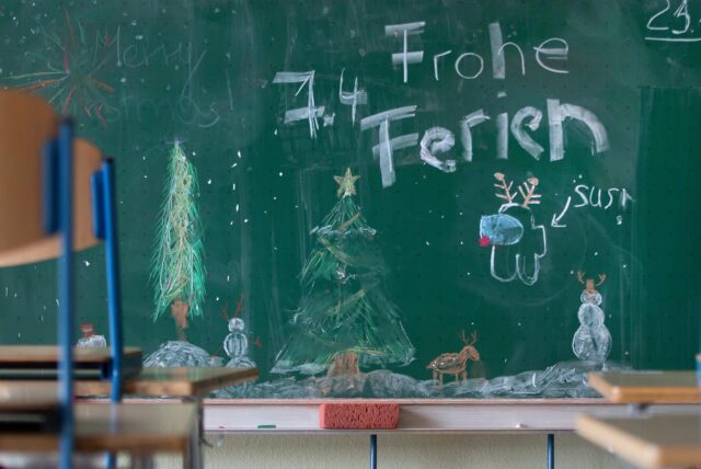 „Frohe Ferien“ steht auf einer Tafel in einem Klassenzimmer über einer winterlichen Zeichnung.