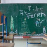 „Frohe Ferien“ steht auf einer Tafel in einem Klassenzimmer über einer winterlichen Zeichnung.