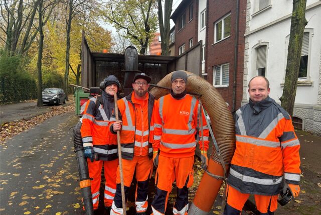 Vier Mitarbeiter des Kommunalen Servicedienst Datteln stehen in orangenen Uniformen vor einem Fahrzeug mit einen Laubsauger.