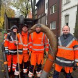 Vier Mitarbeiter des Kommunalen Servicedienst Datteln stehen in orangenen Uniformen vor einem Fahrzeug mit einen Laubsauger.