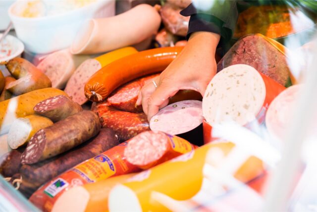 Eine Verkäuferin nimmt Wurst aus einer Theke.