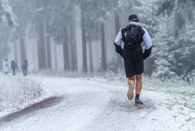 Ein Trailrunner läuft in kurzer Hose auf einem schneebedeckten Waldweg Richtung Feldberggipfel. 