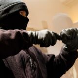 Ein vermummter Mann versucht, ein Fenster oder eine Glastür aufzuhebeln.