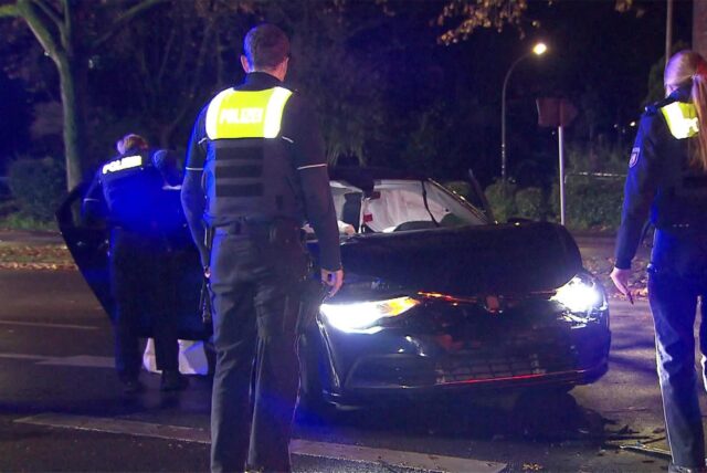 Polizisten stehen neben einem beschädigten Auto.