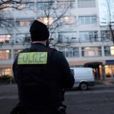 Ein Polizist hat der Kamera den Rücken zugedreht und steht vor einem großen Gebäude.