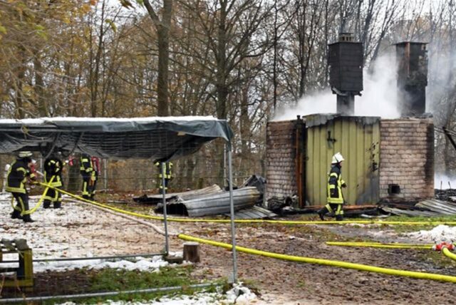 Mehrere Einsatzkräfte vor einem niedergebrannten Gebäude.
