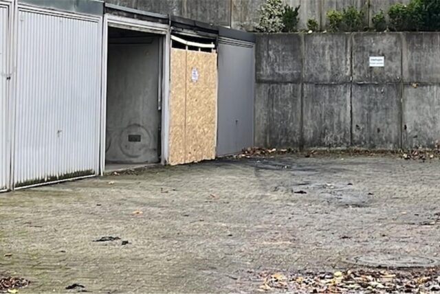 Ein Garagenhof. Eine Garage steht offen, eine andere ist nach einem Brand mit Holzplatten versiegelt.
