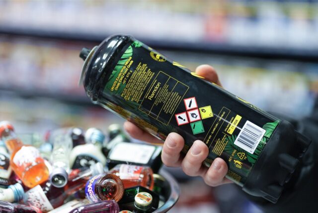 Ein Mitarbeiter hält eine Dose Lachgas am Tresen eines Kiosks in der Hand.