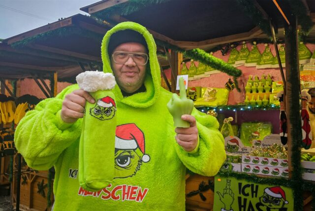 Christoph Scheiding steht in einem neongrünen Hoodie mit der Aufschrift „Ich hasse Menschen“ vor seinem Stand auf dem Dortmunder Weihnachtsmarkt.
