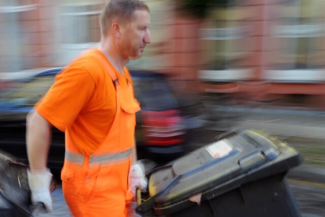 Ein Müllwerker schiebt Tonnen über die Straße.