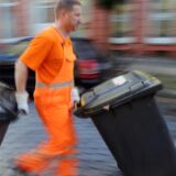 Ein Müllwerker schiebt Tonnen über die Straße.