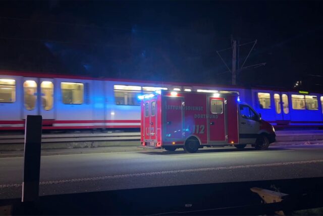 Ein Rettungswagen steht neben einer fahrenden Stadtbahn.