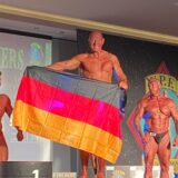 Bodybuilder Jörg Rode hält bei der Siegerehrung eine Deutschlandfahne hoch.