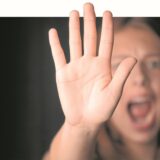 Eine schreiende Frau erhebt ihre Hand zur Abwehr.