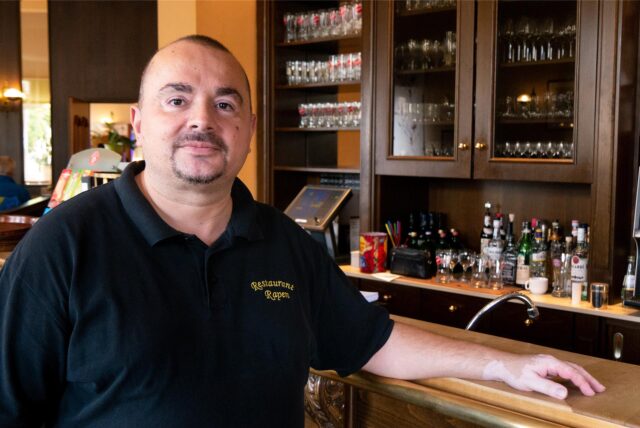 Ein Mann in schwarzem Poloshirt steht an der Bar eines Restaurants in Oer-Erkenschwick. Der linke Arm ist auf den Tresen gestützt.