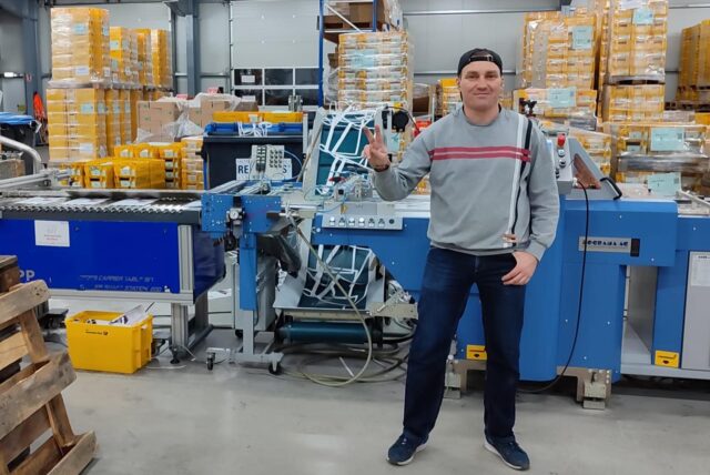 Ein Mann in grauem Pullover steht vor einem Förderband in der Firma Wirtz Druck in Datteln.
