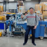 Ein Mann in grauem Pullover steht vor einem Förderband in der Firma Wirtz Druck in Datteln.