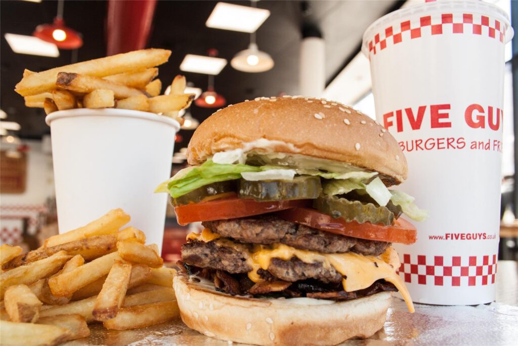 Ein Burger von „Five Guys“ liegt neben einer Portion Pommes und einem Getränkebecher.