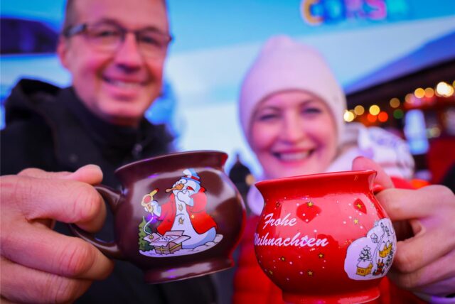 Ein Paar hält zwei Tassen mit heißem Glühwein kurz nach der Eröffnung des „Santa Pauli“ Weihnachtsmarkt“ auf dem Spielbudenplatz.